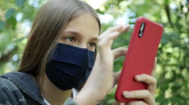 Koronavirüs salgını nedeniyle koruyucu maskeli hasta çocuk, akıllı telefondan internete bakan çocuk, akıllı telefon oynayan kız.