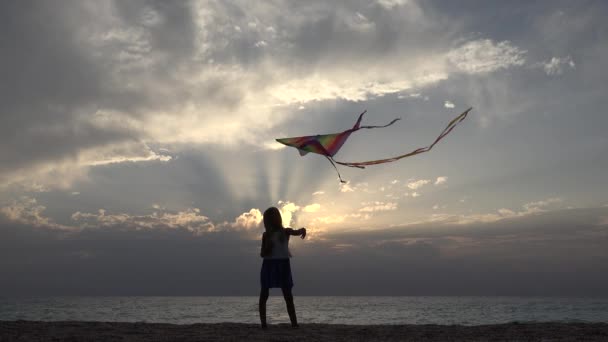 Menina brincando na praia na costa, Kid Flying Kite ao pôr do sol no oceano, Chid na costa em férias de verão, ondas do mar — Vídeo de Stock