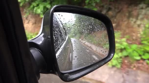 Автомобиль в дождь на городской дороге, водитель за рулем автомобиля в сильный шторм на шоссе, дождевые капли на зеркало заднего вида, наводнение — стоковое видео