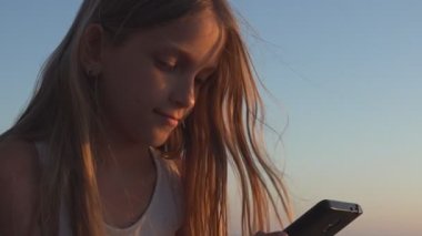 Akıllı Telefon Oynayan Çocuk, Gün Batımında Sahilde Çocuk, Yaz Tatili 'nde Gün batımında Deniz kenarında Tablet Kullanan Genç Sarışın Kız