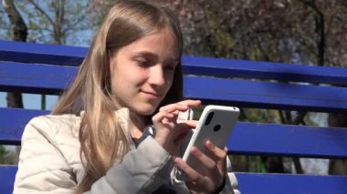 Parktaki Smartphone 'da Çocuk Tarayıcısı, Genç Çocuk Bench' te Açık Alan Cihazları, Akıllı Telefon Oynayan Ergen Kız