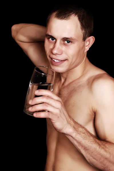 Muscular young man with glass of water on black background — Stock Photo, Image