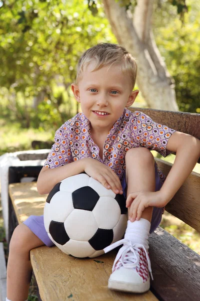 Ładny chłopiec z piłką, siedząc na ławce — Zdjęcie stockowe
