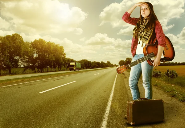 Yong flicka med guitare och gammal resväska på motorvägen — Stockfoto