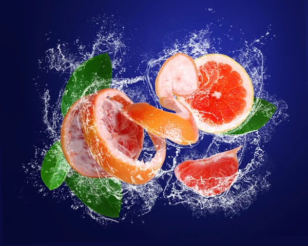 Grapefruit und Stücke mit Blättern in Spritzwasser — Stockfoto