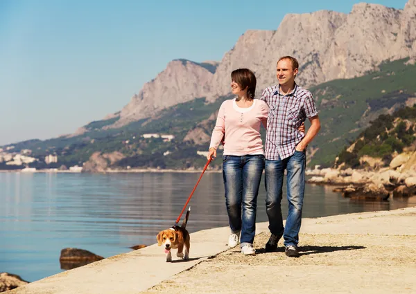Happy couple walking with puppy on the seacoast — Stock Photo, Image