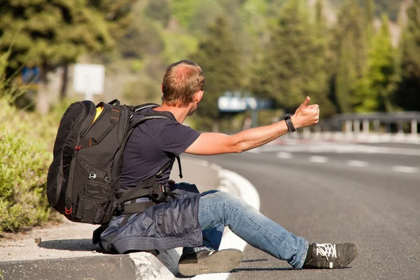 Autostopem człowiek samotnie siedzący na poboczu drogi — Zdjęcie stockowe