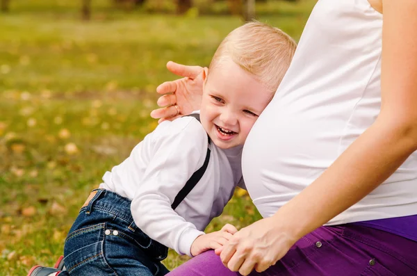Gelukkig glimlachend kind in de buurt van zwangere moeder buik — Stockfoto
