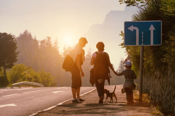 Rodinné backpackers jde na silnici při západu slunce — Stock fotografie