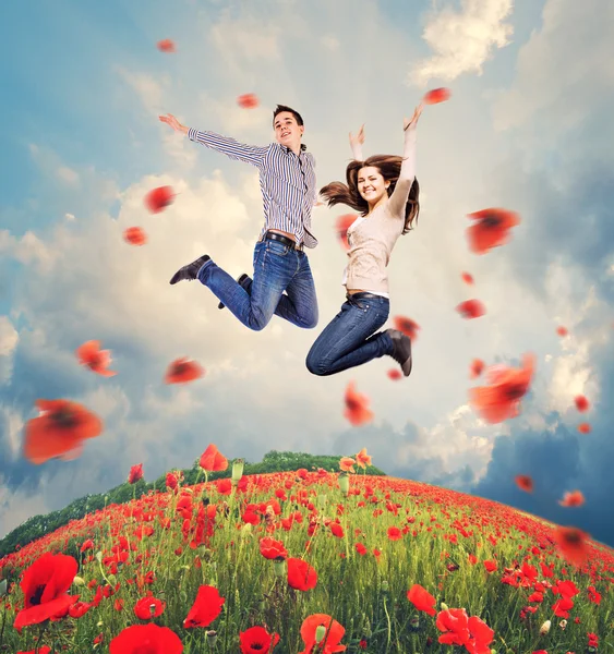 Happy young couple jumping in poppies field — Stock Photo, Image