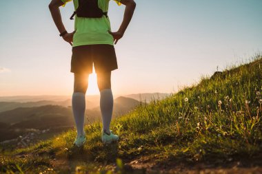 Aktif dağ koşucusunun güneş batarken pikoresk tepelerde koşarken sırt çantalı parlak tişörtü giyip günbatımının tadını çıkarışının arka planı. Sportif aktif insanlar veya motivasyon kavramı