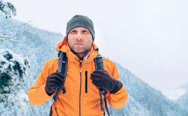 Sırt çantalı parlak turuncu kabuklu adam kış dağları rotasında yürüyüş yapıyor. Aktif insanlar ya da doğa konseptinde hayatta kalma imajı..