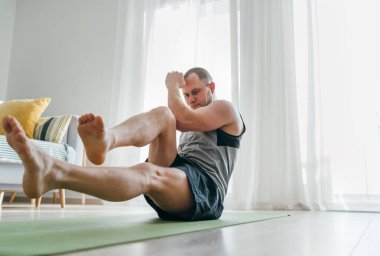 Bisiklet yapan genç kaslı vücut adam oturma odasında kaslarını çalıştırıyor. Sağlıklı yaşam tarzı ya da sporcu imajı.