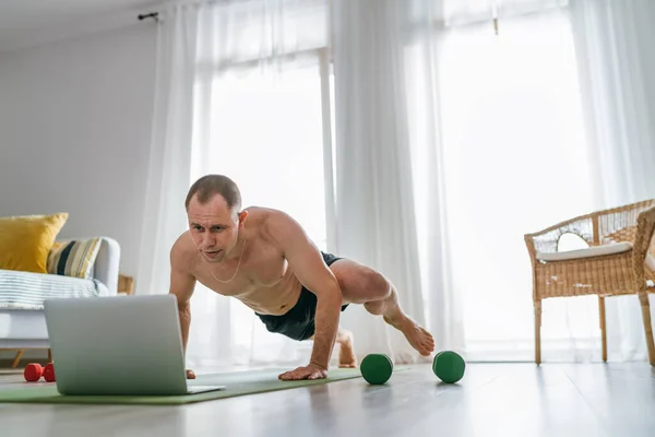 客厅里的家庭锻炼 年轻的肌肉男在网上做蜘蛛人俯卧撑跟踪健身教练使用笔记本电脑 健康的生活方式和现代在线技术概念 — 图库照片
