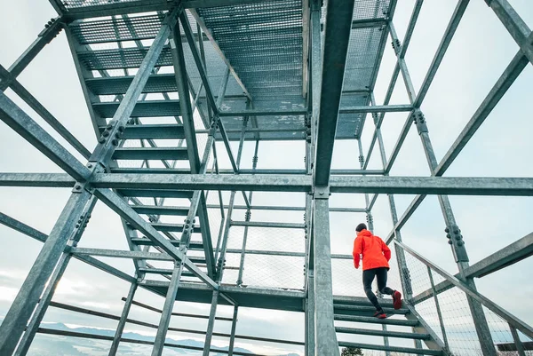 寒い冬の日に巨大な鉄鋼産業用階段で駆け上がる明るい赤のソフトシェルのスポーティーな服を着たランナーの男だけ 人々の健康的なライフスタイルのコンセプト写真 — ストック写真