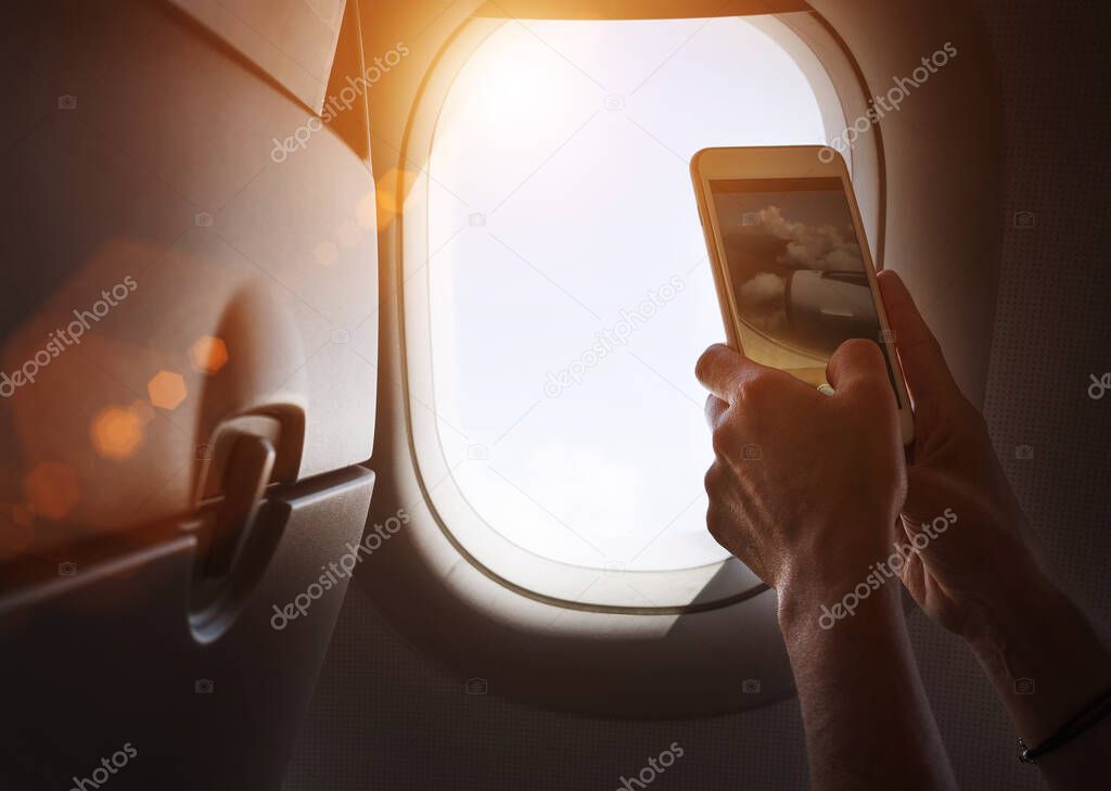 Female using her smartphone for photographing clouds and aircraft engine through the porthole. Active traveling and flying by planes aviation transport concept image.