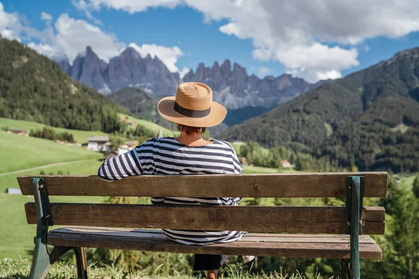 意大利南蒂罗尔Val Funes山谷 穿着草帽的年轻时尚女性坐在长椅上 欣赏着圣诞老人玛达莱纳村的景色和迷人的风景如画的白云石阿尔卑斯山峰 — 图库照片