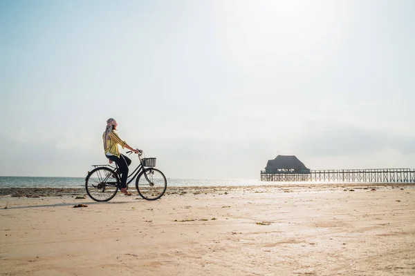坦桑尼亚桑给巴尔岛Kiwengwa海滩上 身着浅色夏装的年轻女性骑着老式自行车 前篮放在孤独的低潮大海白沙滩上 — 图库照片