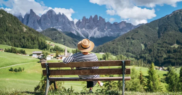 意大利南蒂罗尔Val Funes山谷 穿着草帽的年轻时尚女性坐在长椅上 欣赏着圣诞老人玛达莱纳村的景色和迷人的风景如画的白云石阿尔卑斯山峰 — 图库照片