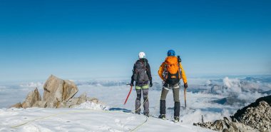 Çift halatı tırmanma takımına bağlı. Sırt çantaları ve buz baltalarıyla dağcılık kıyafetleri giyip Fransa 'nın Aiguille du Midi kenti yakınlarındaki Monte Bianco zirvesinde Mont Blanc' ın (Monte Bianco) manzarasının keyfini çıkarıyorlar..