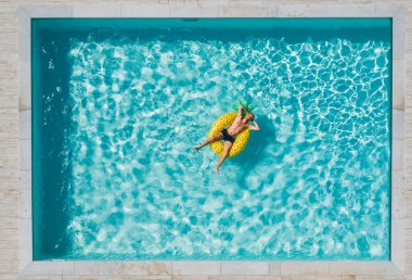 Güneş gözlüklü, neşeli orta yaşlı bir adam mavi yüzme havuzunda yüzüyor, dev şişme sarı ananas tüpünde ve gülüyor. Lüks tatil beldelerinde yaz tatili konsepti..