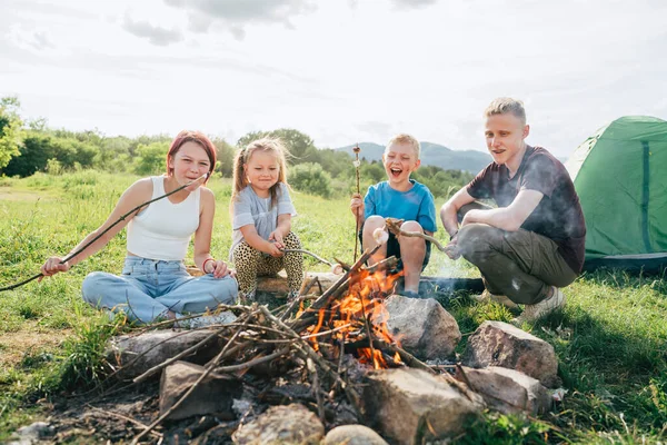 男孩和女孩们在靠近绿色帐篷的篝火上欢快地笑着 在树枝上烤棉花糖和腊肠 户外活动时间或露营自然概念 — 图库照片