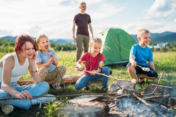 男の子と女の子の友人子供たちは 緑のテントの近くのキャンプファイヤーの炎の上に棒でマシュマロを陽気に笑って焙煎します アウトドアアクティブ時間自然コンセプトで過ごすか キャンプ — ストック写真