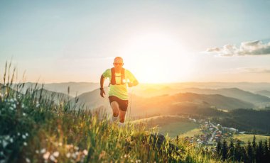 Aktif dağ koşucusu güneş gözlüklü sırt çantalı parlak bir tişört giyerek gün batımında pitoresk tepelerin yanından geçerek dayanıklılık maratonu yapıyor. Sportif aktif insanlar konsept imajı.