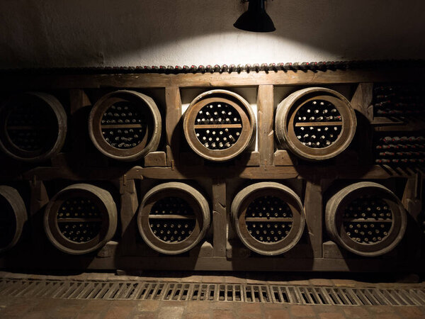 Wine cellar low light interior shot. Old wooden shelves with a collection of wine bottles. Money investing and winemaking or consumption concept image.