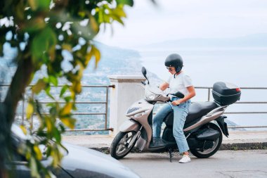 Kasklı orta yaşlı bir kadın ve motosikletli güneş gözlüklü bir kadın Forza d 'Agro' daki Sicilya 'nın eski caddelerinde Sant' Alessio Siculo limanında. Mutlu İtalyan tatili ve ulaşım konsepti. 