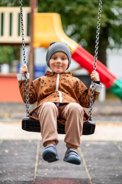 Mutlu küçük çocuk sonbaharda çocuk parkında sallanıyor.