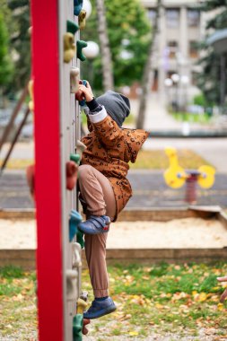 Küçük çocuk kaya duvarına tırmanıyor ve oyun alanında oynuyor.
