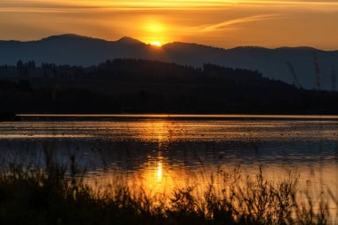 Dağların üzerinden gün batımı. Su yüzeyinde yansıma. Renkli alacakaranlık gökyüzü.