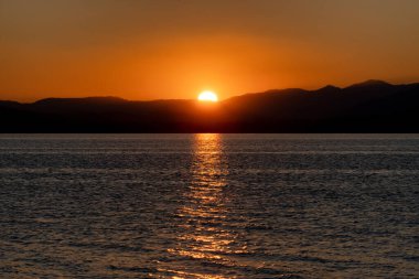 Güneş doğarken renkli su yüzeyi. Arka planda büyük güneş ve dağların silueti var. Slovakya 'daki Liptovska Gölü Mara