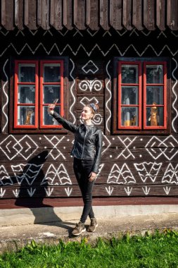 Siyahlı genç kız Slovakya 'nın kırsal kesimindeki Cicmany köyünün eski kır evinin önünde selfie çekiyor.