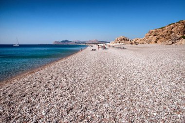 TRAGANOU, GREECE - JULY 1, 2022: Vacationers relaxing at pebble Traganou beach at Rhodes island in Greece