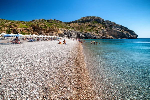 TRAGANOU, GREECE - JULY 1, 2022: Vacationers relaxing at pebble Traganou beach at Rhodes island in Greece