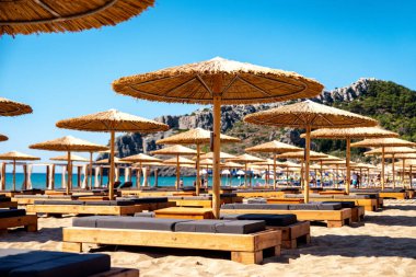 TSAMBIKA, GREECE - JULY 2, 2022: Loungers under sunshades ready for vacationers in Tsambika beach at Rhodes island in Greece