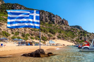 TSAMBİKA, GREECE - 2 Temmuz 2022: Yunanistan 'ın Rodos adasındaki Tsambika plajında Yunan bayrağı sallamak