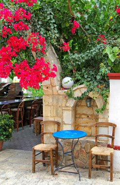 Empty seats and table in taverna under the blooming red flowerd.