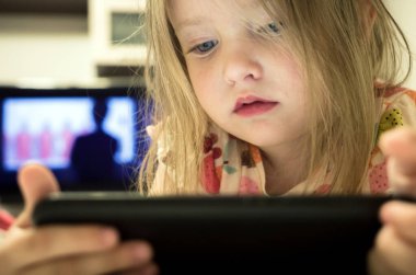 Small baby girl looking on smartphone and television. Mobile phone addiction in kid concept.