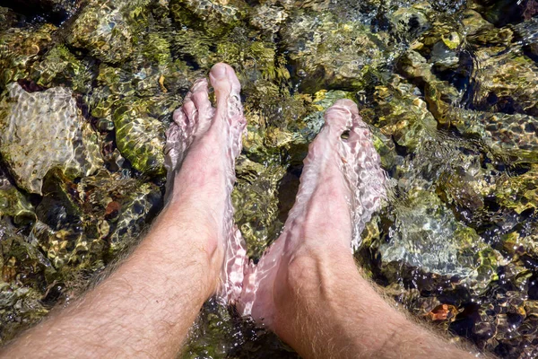 Male feet immersed in the clear water of a mountain stream. Cooling off on a hot day.