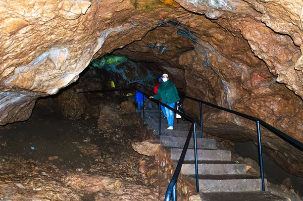 A woman, a member of a tourist group, poses against the backdrop of a cave.
