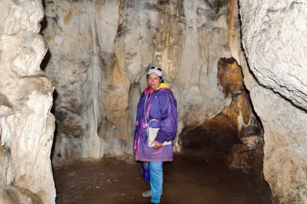 A woman, a member of a tourist group, poses against the backdrop of a cave. Emine-Bair Khosar cave. Mammoth karst cave.