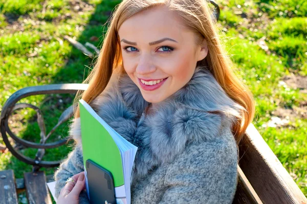 Young female student sits on a park bench hanging books — Stock Photo, Image