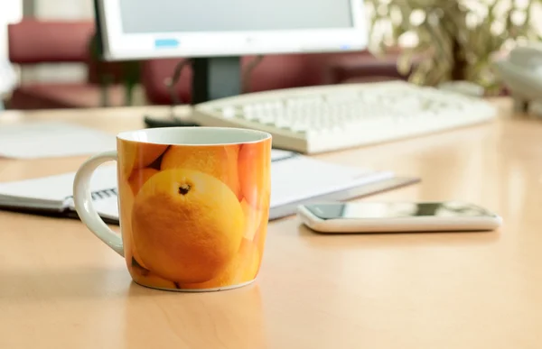 Kopp te på tabellen office med smartphone i närheten — Stockfoto