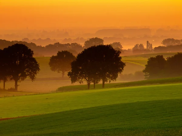Oranje zonsopgang boven mistige en heuvelachtig landbouwgrond — Stockfoto