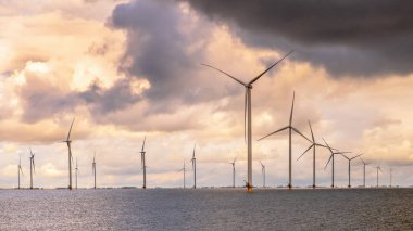 Denizdeki Windfarm açıklarında. IJsselmeer 'in sularında bulutlu gökyüzünün altında bir grup rüzgar türbini. Rüzgar enerjisi sürdürülebilirliğe giden yeşil tepside elektriğin en ucuz formlarından biri haline geldi. Hollanda.