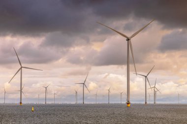 Denizdeki Windfarm açıklarında. IJsselmeer 'in sularında bulutlu gökyüzünün altında bir grup rüzgar türbini. Rüzgar enerjisi sürdürülebilirliğe giden yeşil tepside elektriğin en ucuz formlarından biri haline geldi. Hollanda.