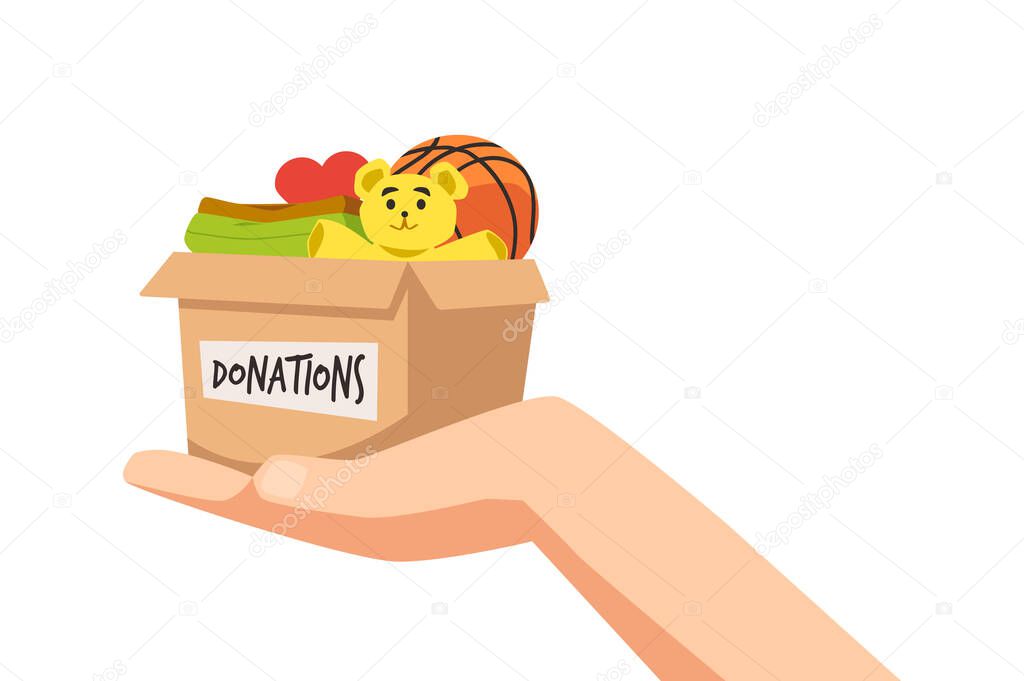 Hand holding donation paper box with toys and clothes, flat vector illustration isolated on white background. Donation box with teddy bear and basketball ball, charity for children and orphans.